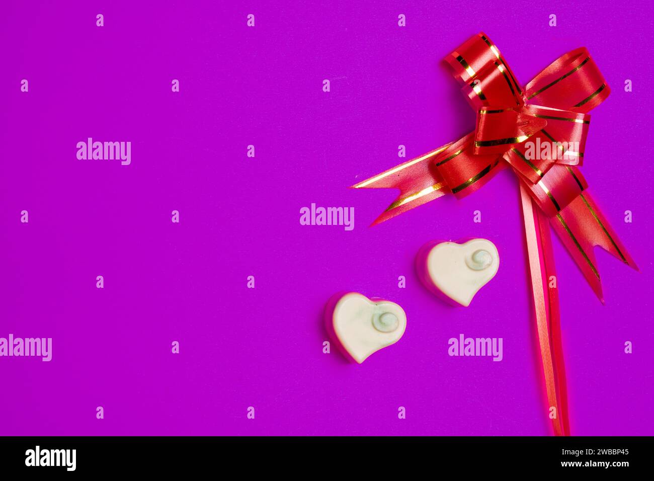 two heart-shaped chocolates and a gift bow on a purple background Stock Photo