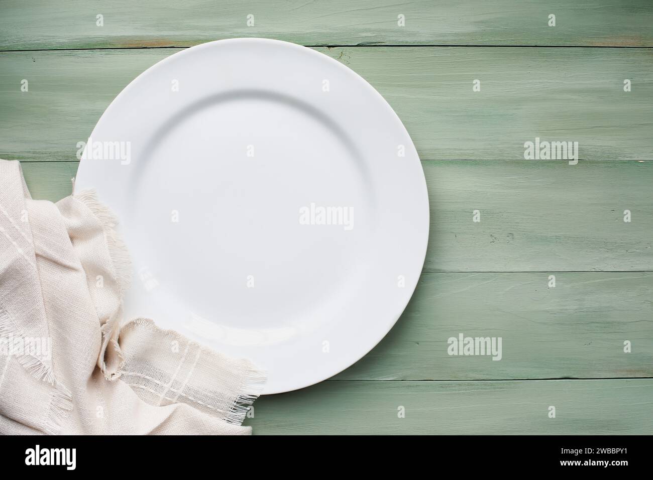 An empty white plate with napkin over a rustic green spring table, shot from flat lay or table top view position. Free space for text. Stock Photo