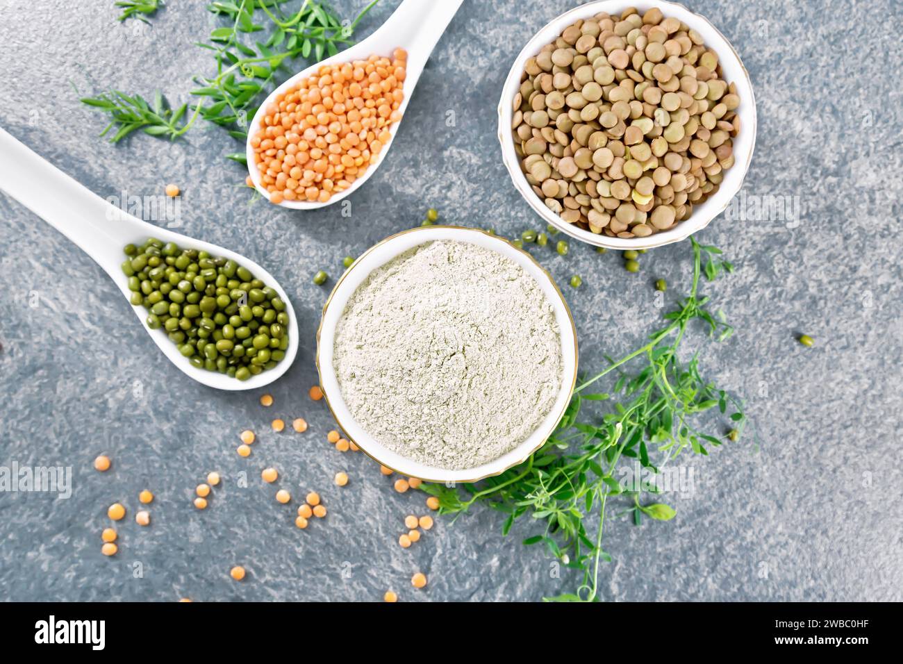 Lentil flour in a bowl, red, green lentils in spoons, brown in a bowl, bean stalks with leaves on the background of granite table from above Stock Photo