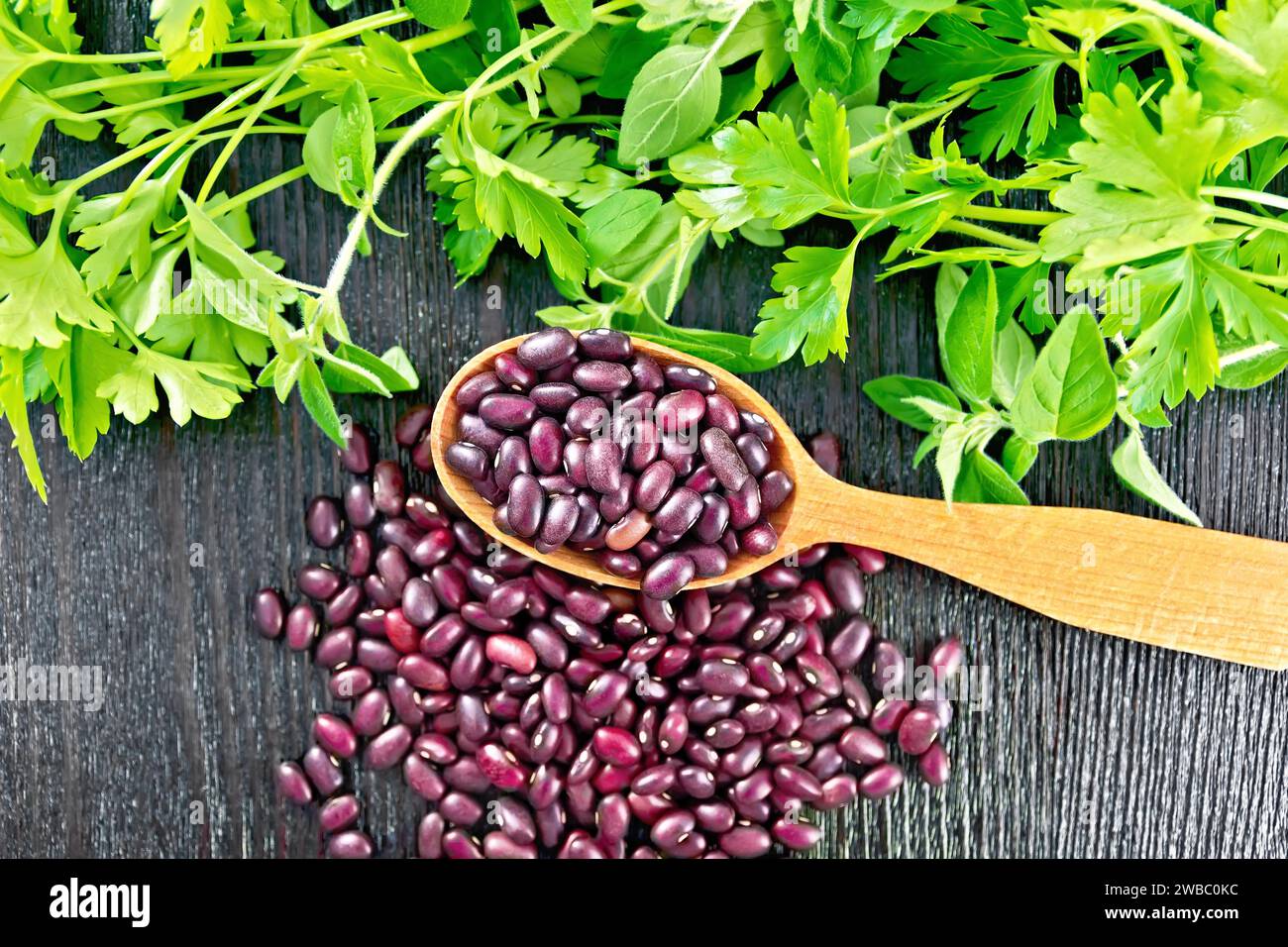 Ruby haricot in a spoon and on the table, parsley and oregano on a wooden board background from above Stock Photo