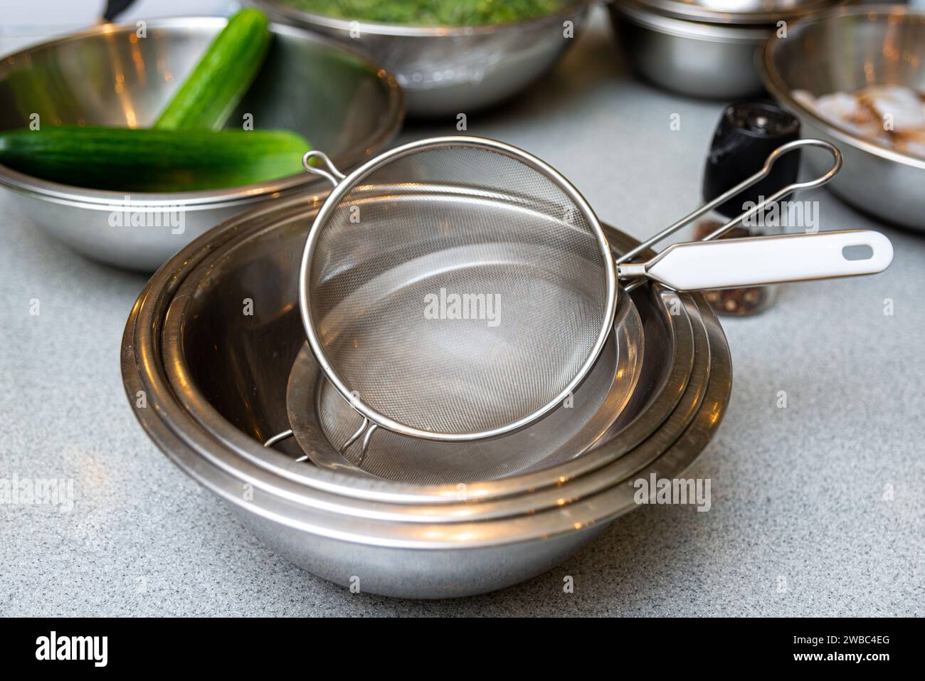 A stainless steel mesh strainer atop mixing bowls with fresh cucumbers