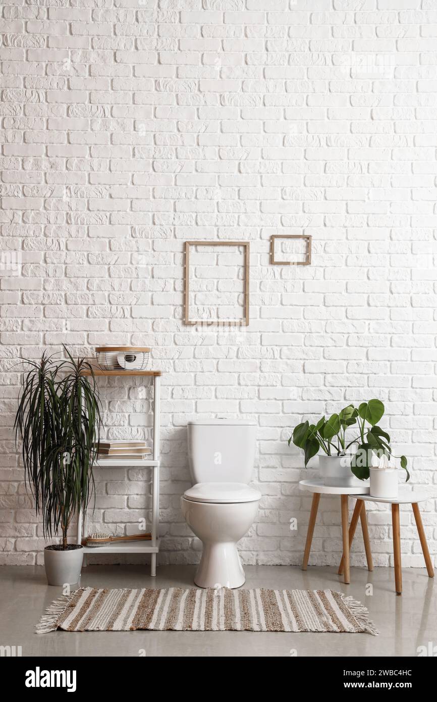 Interior of light restroom with ceramic toilet bowl, shelving unit and ...