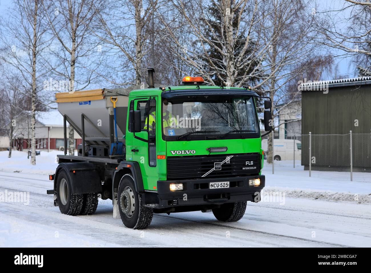 Lime green Volvo FL6 gritting lorry spreading grit on icy and snowy road on a cold day of winter. Salo, Finland. December 27, 2023. Stock Photo