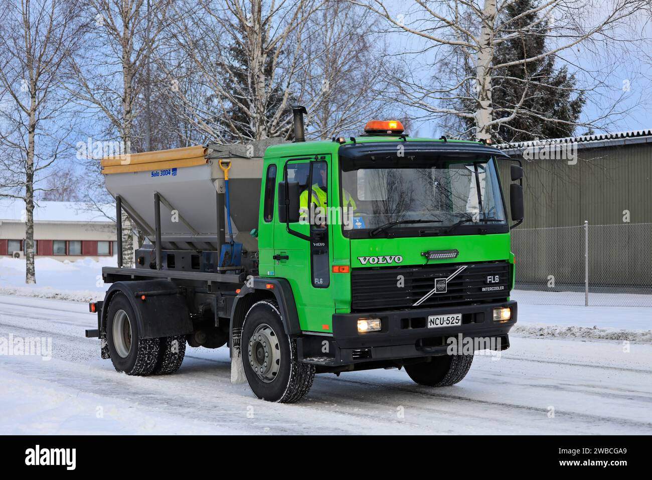 Lime green Volvo FL6 gritting lorry spreading grit on icy and snowy road on a cold day of winter. Salo, Finland. December 27, 2023. Stock Photo