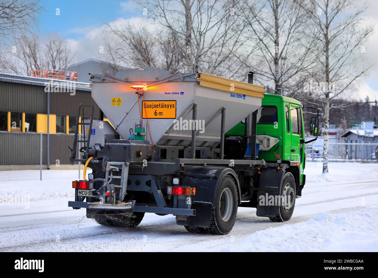 Volvo FL6 gritting lorry spreading grit on icy and snowy road on a cold day of winter, rear view. Salo, Finland. December 27, 2023. Stock Photo