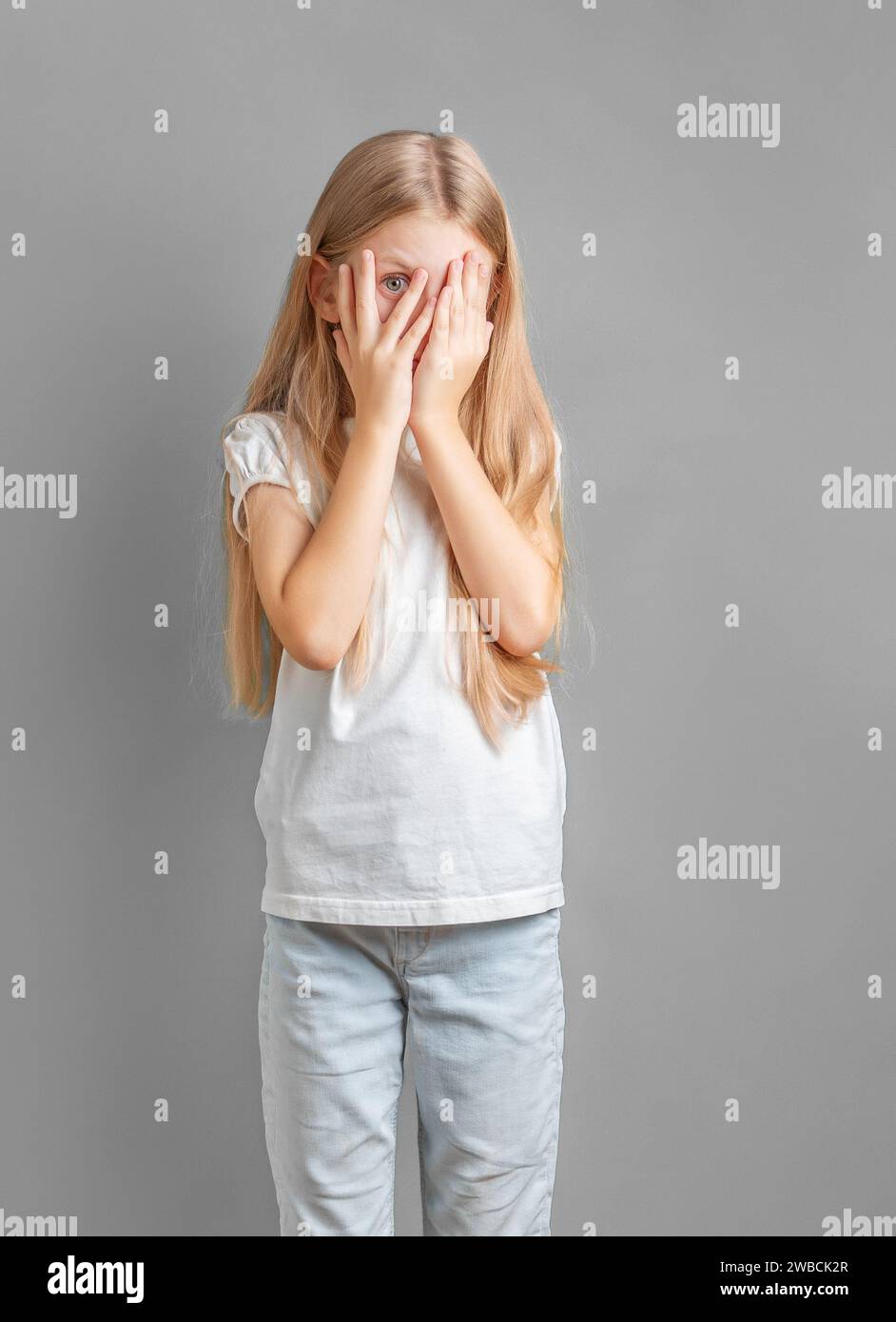 A little girl covering her face with her hands and peeking through her fingers. Stock Photo