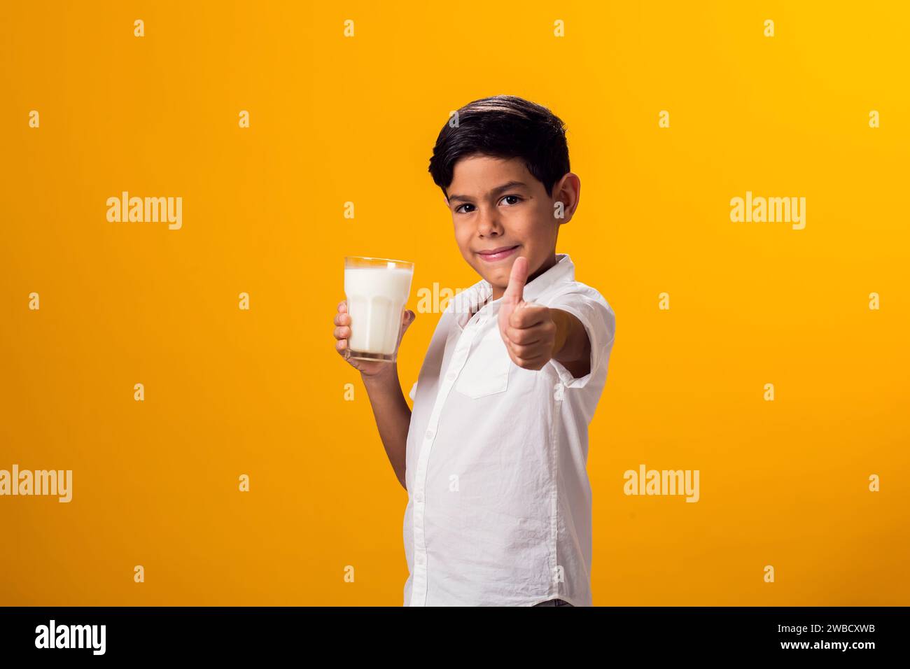 Pjrtrait of happy boy holding glass of milk and showing thumbs up gesture. Nutrition and health concept Stock Photo