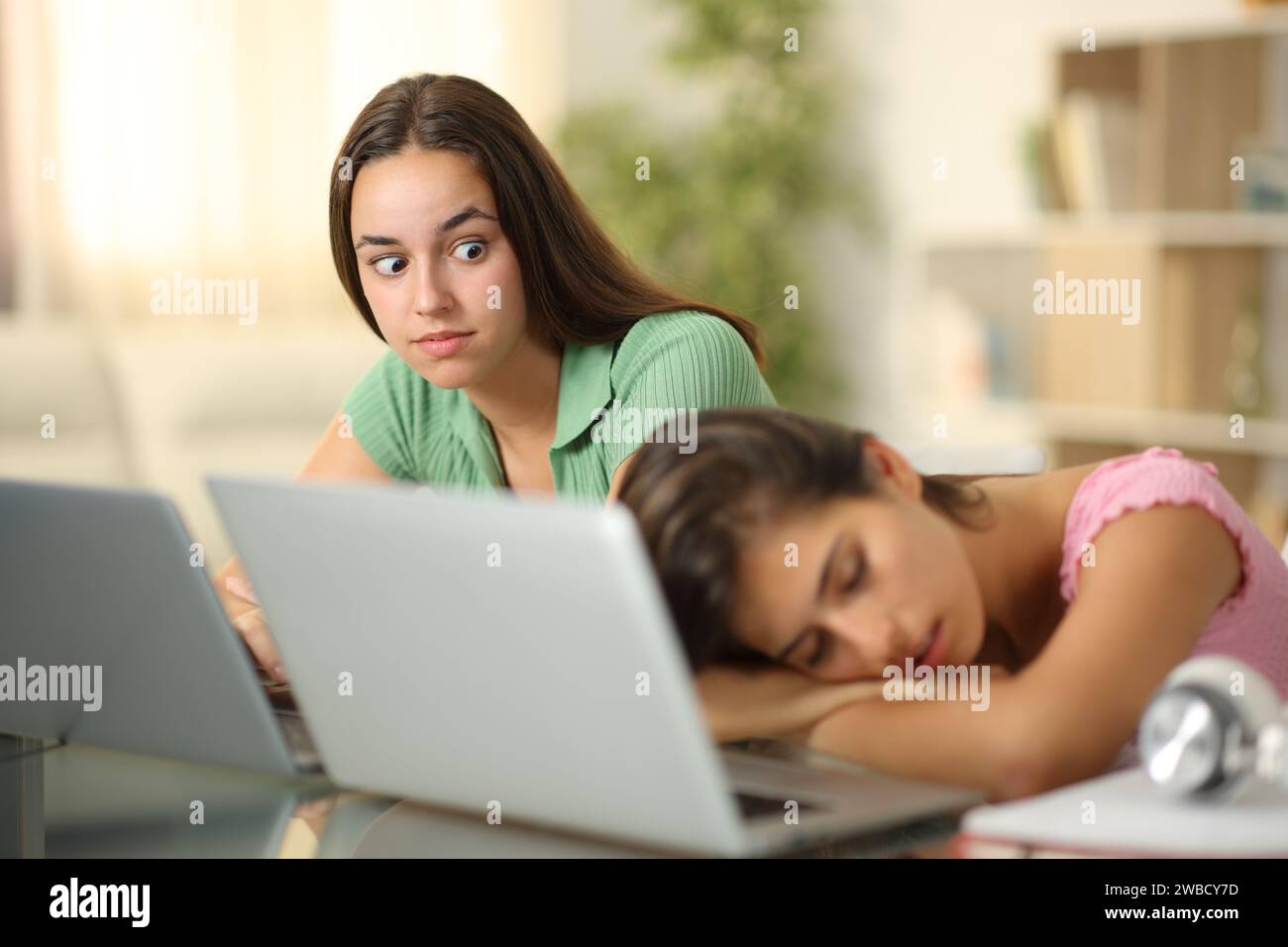 Perplexed student looking at her classmate sleeping at home Stock Photo