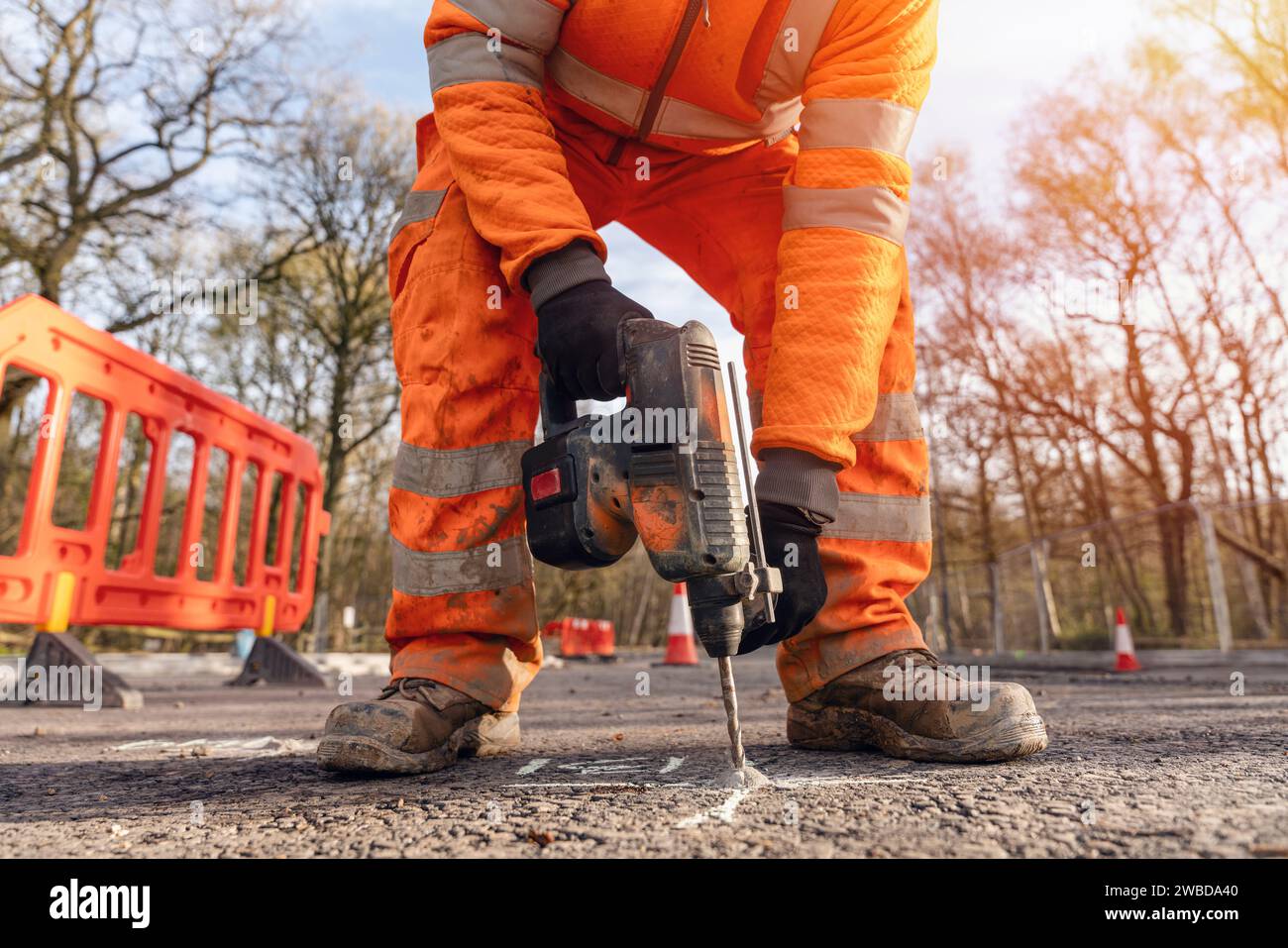 Close-up of a builder using a cordless hammer drill to drill holes in the road at the location marked by the site engineer surveyor Stock Photo