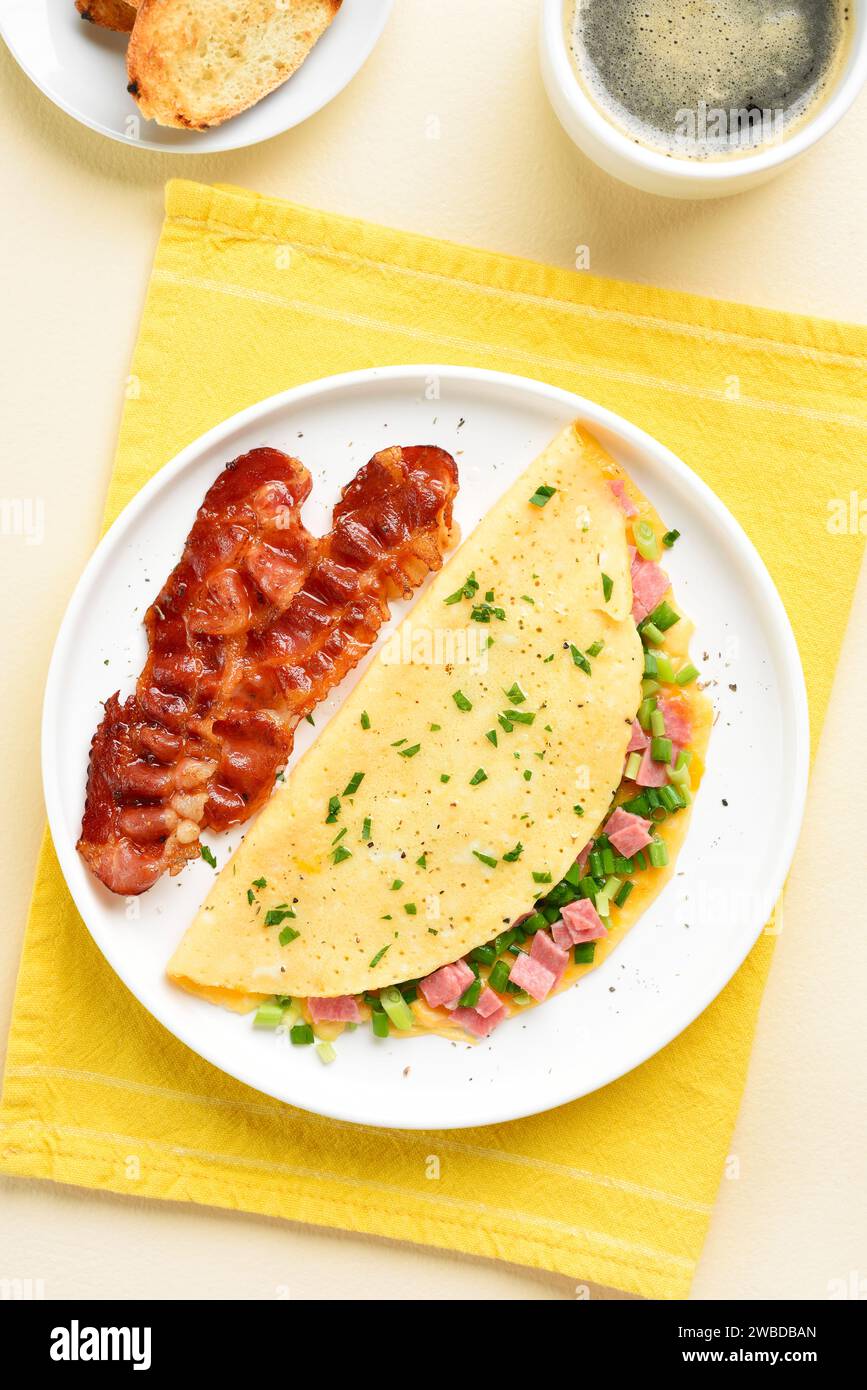 Omelet with ham, green onion, roasted bacon and cup of coffee over light background. Top view, flat lay. Stock Photo