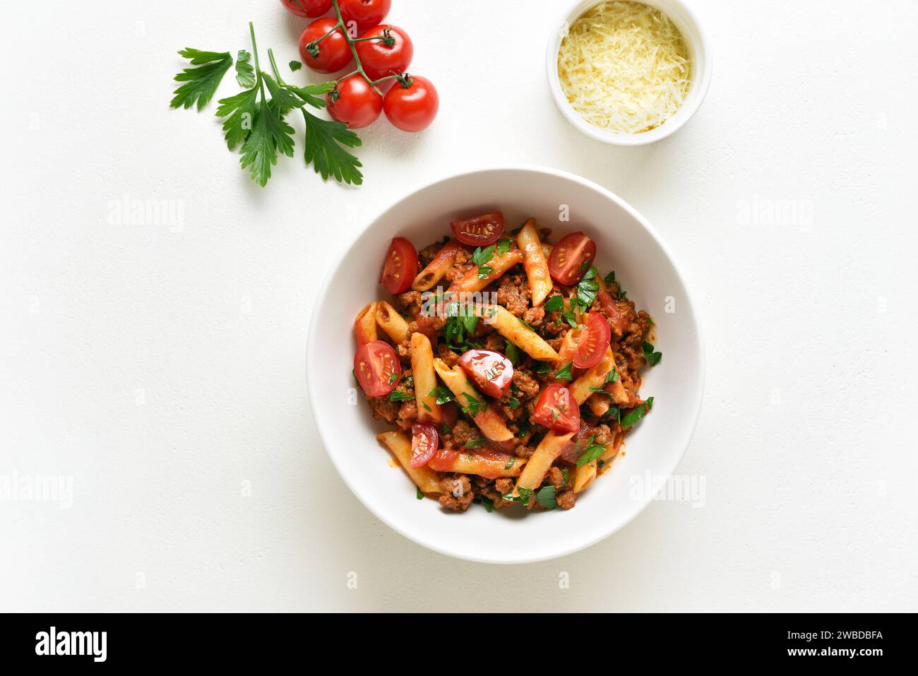 Bolognese penne pasta with minced meat, tomatoes and greens in bowl over white background with copy space. Top view, flat lay Stock Photo