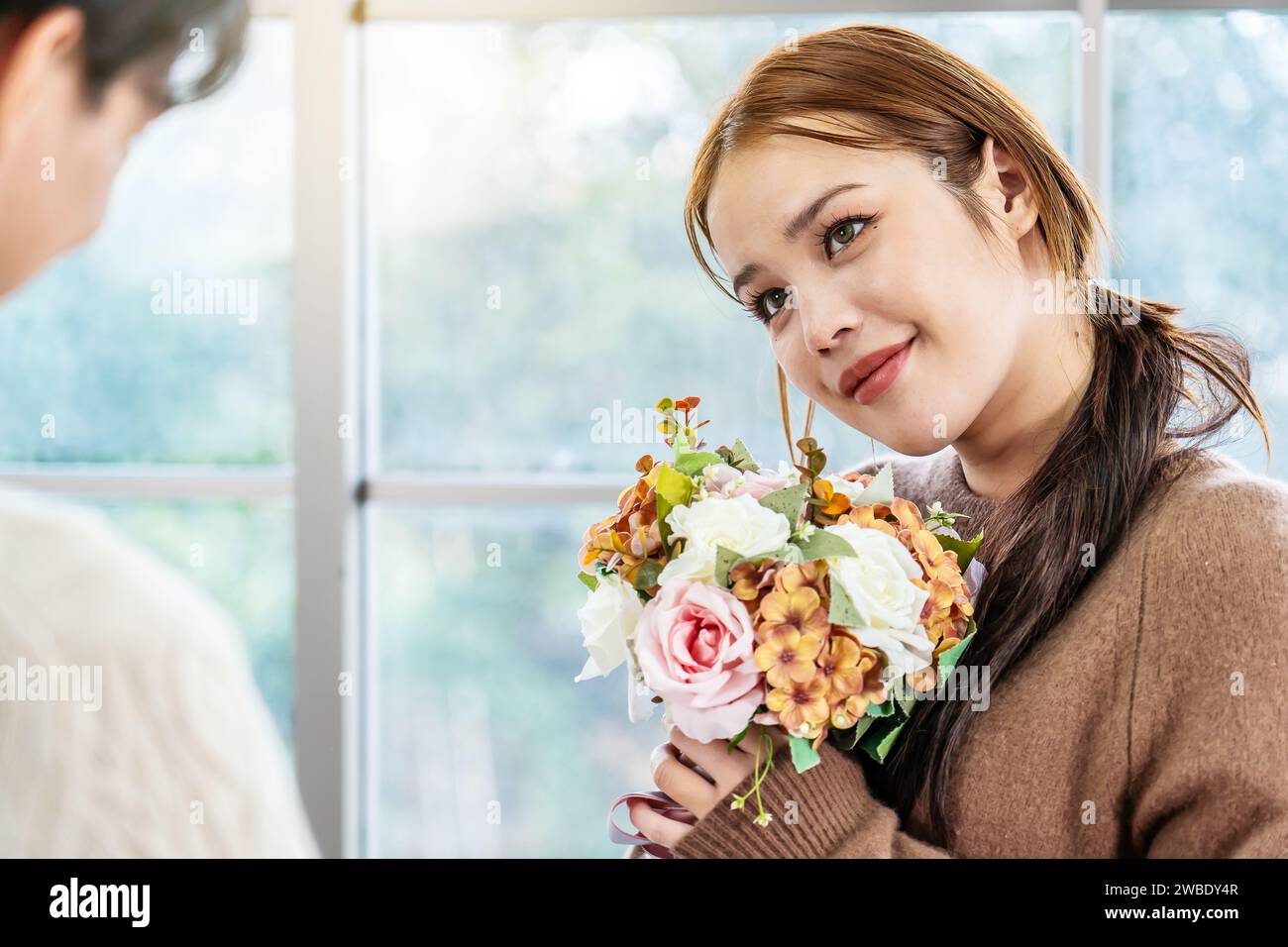 Asian young man surprising his beautiful girlfriend with bouquet of flowers at home, Attractive romantic new marriage couple male and woman Stock Photo