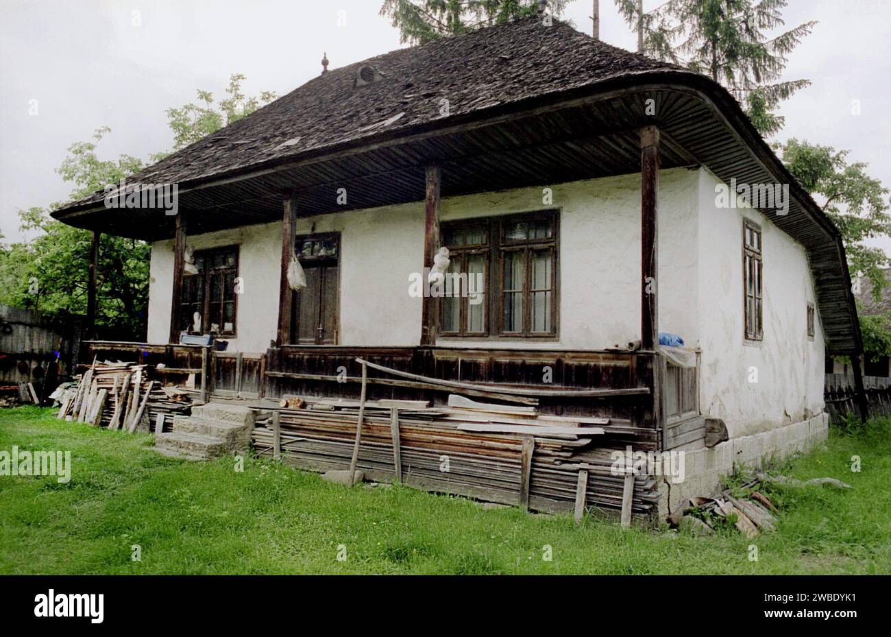 Vrancea County, Romania, approx. 1995. A traditional house with wooden roof in poor condition. Timber stacked in the yard. Stock Photo