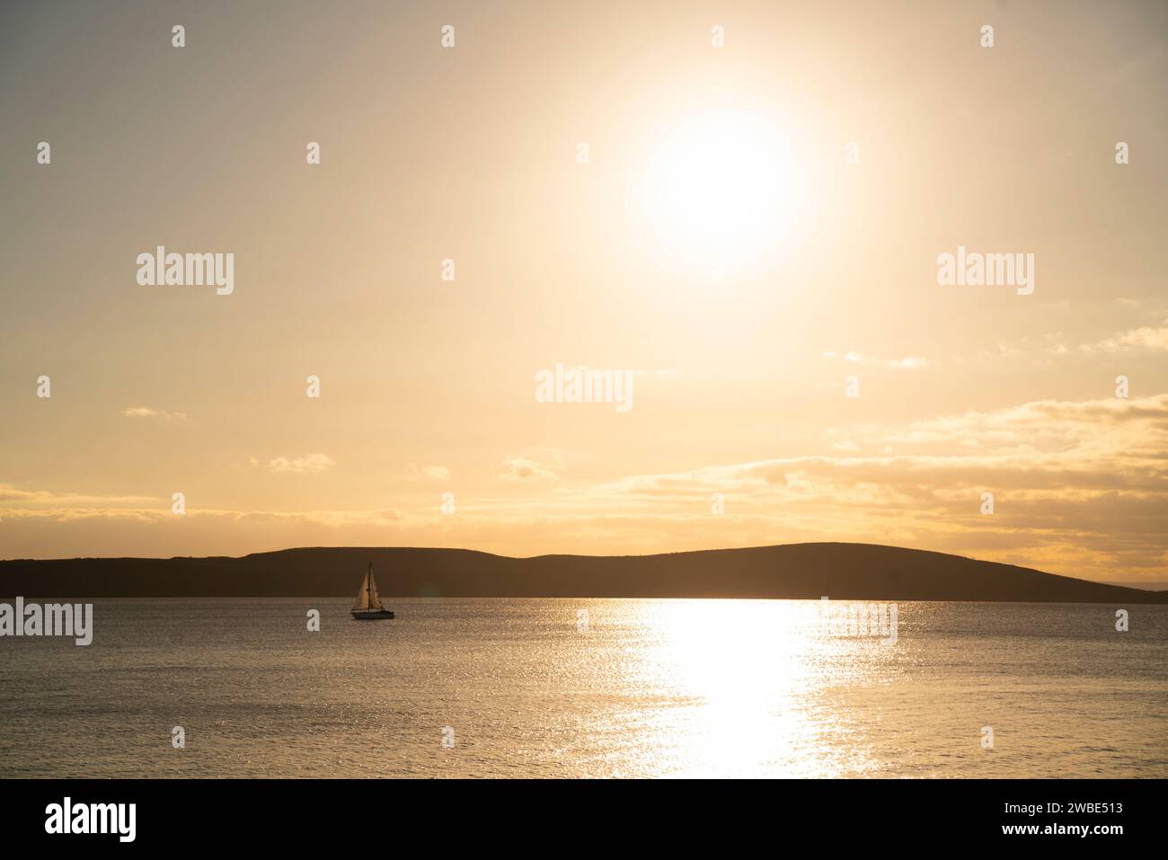 A sailing boat sails across the bay of Weston-super-Mare, North Somerset with Brean Down in the background at sunset. Stock Photo