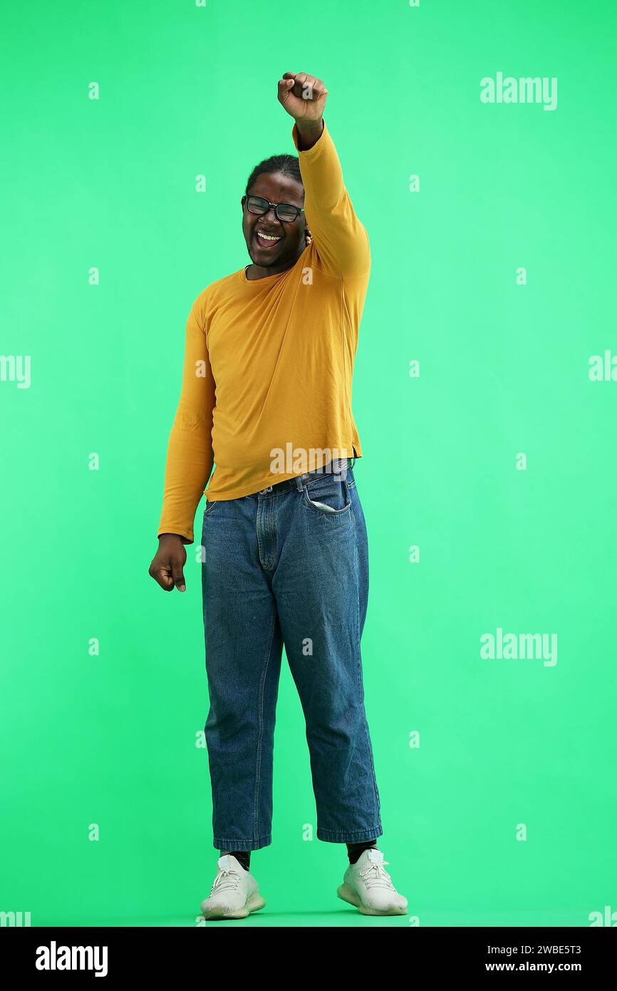 A man in a yellow jacket on green background raised his hand up Stock Photo