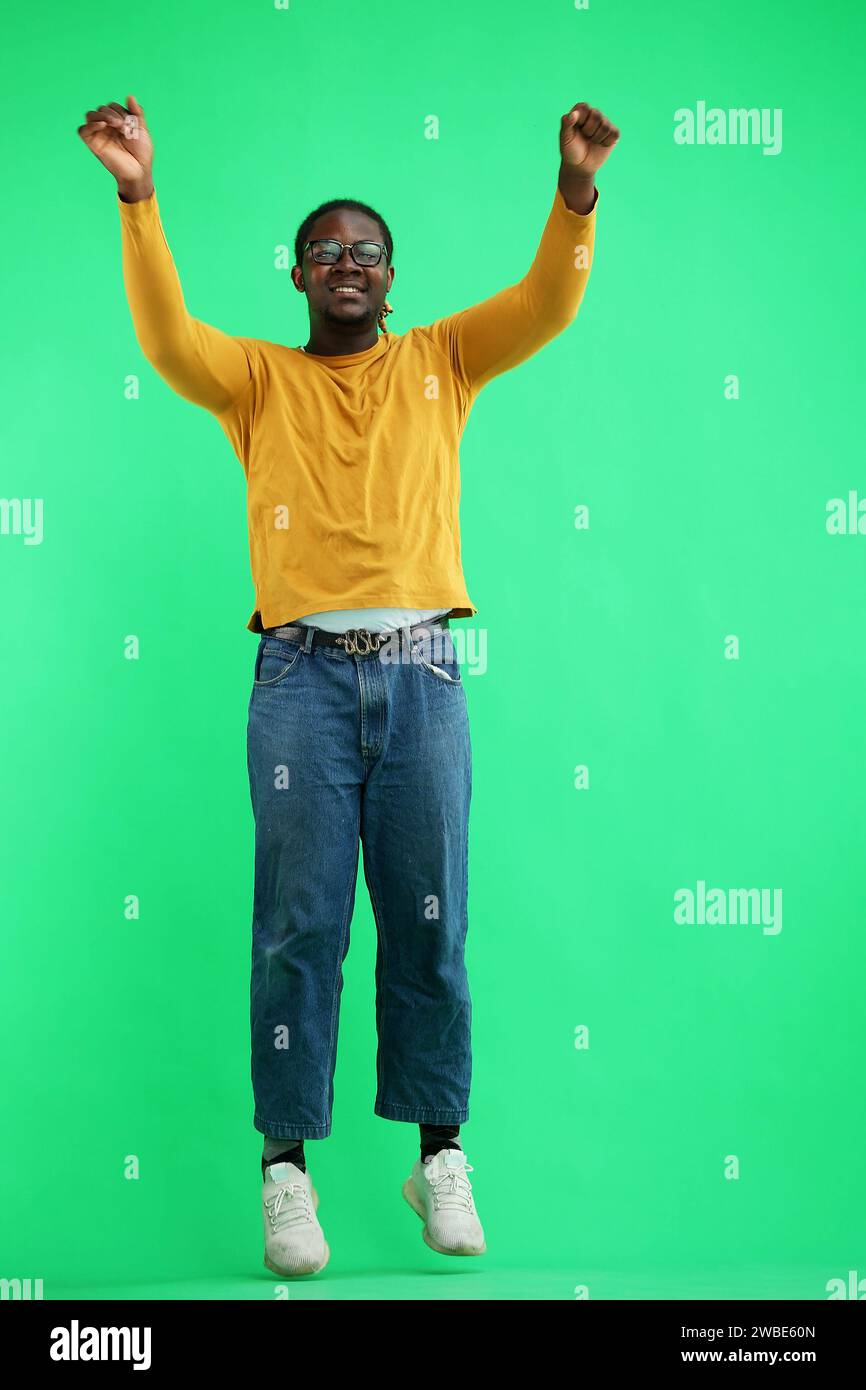 A man in a yellow jacket jumps on a green background Stock Photo