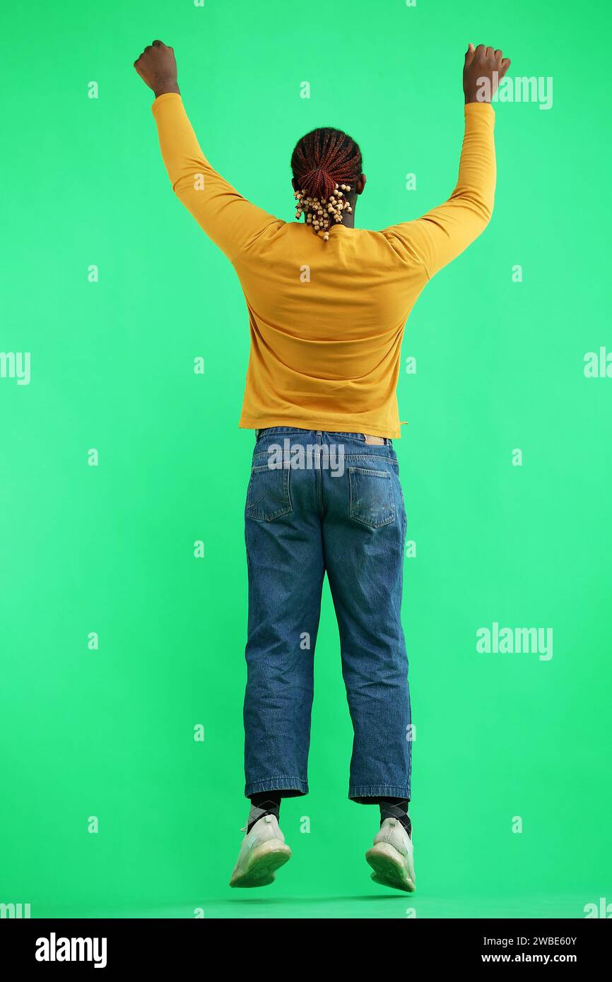 A man in a yellow jacket jumps on a green background, back view Stock Photo