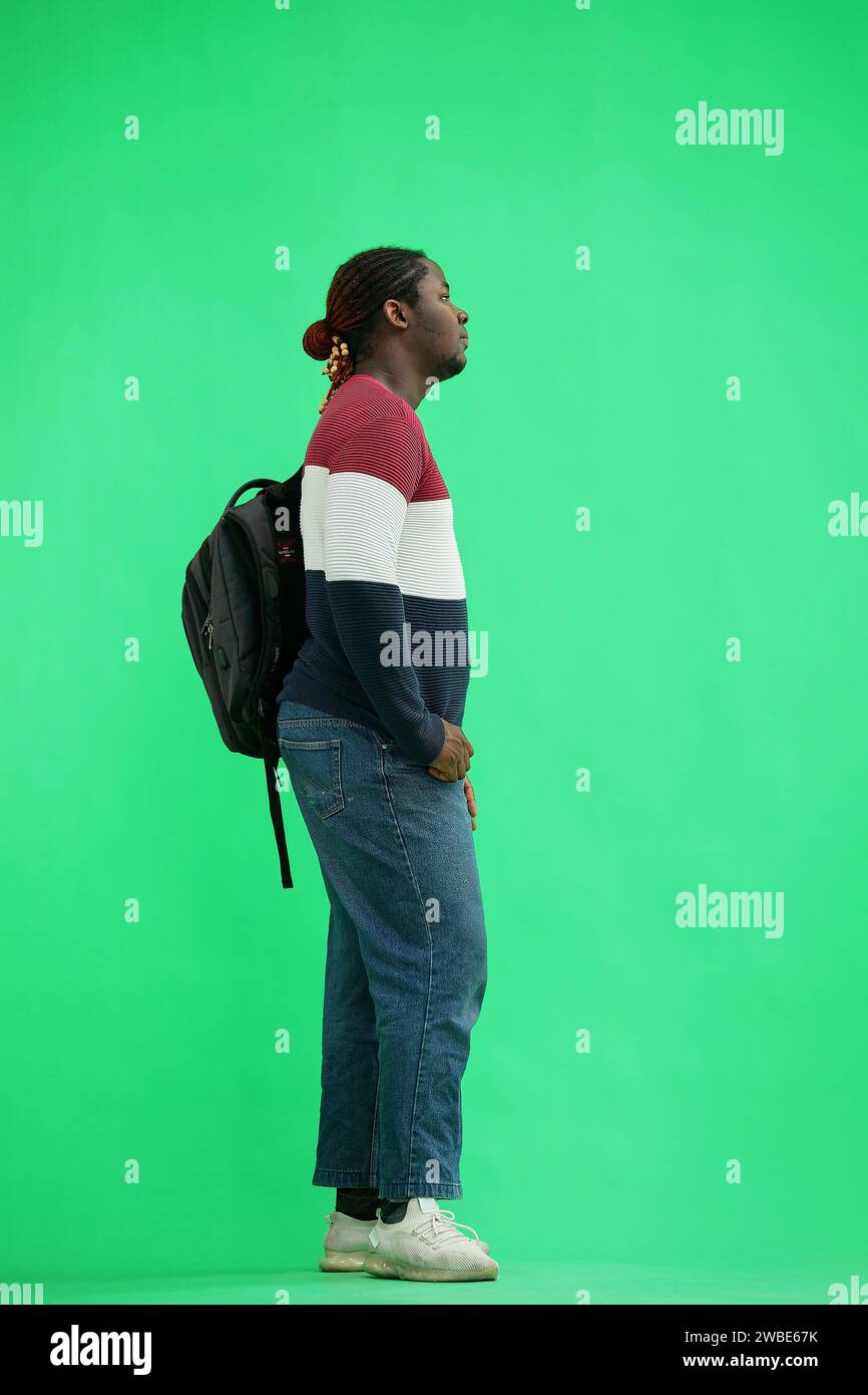 A man in a multi-colored jacket with a backpack on a green background, in profile Stock Photo