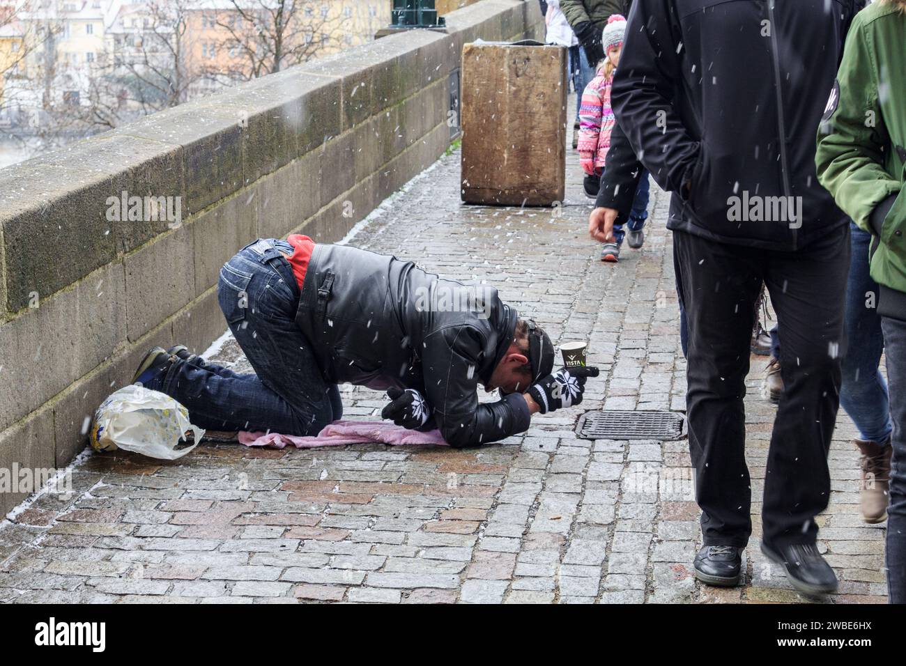 Photo of a beggar on the Charles bridge in Prague. It was taken on a cold winter day. He is begging for money on his knees while people are going Stock Photo