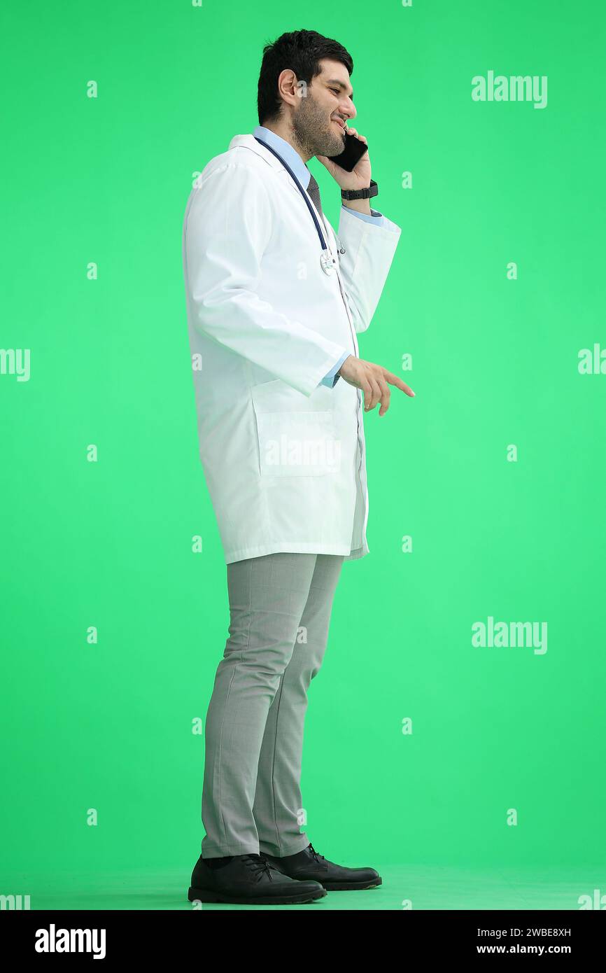 Male doctor on a green background in full growth talking on the phone, in profile Stock Photo
