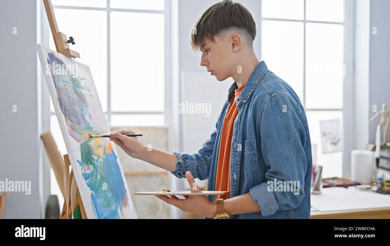 A focused young man paints on a canvas in a bright art studio ...