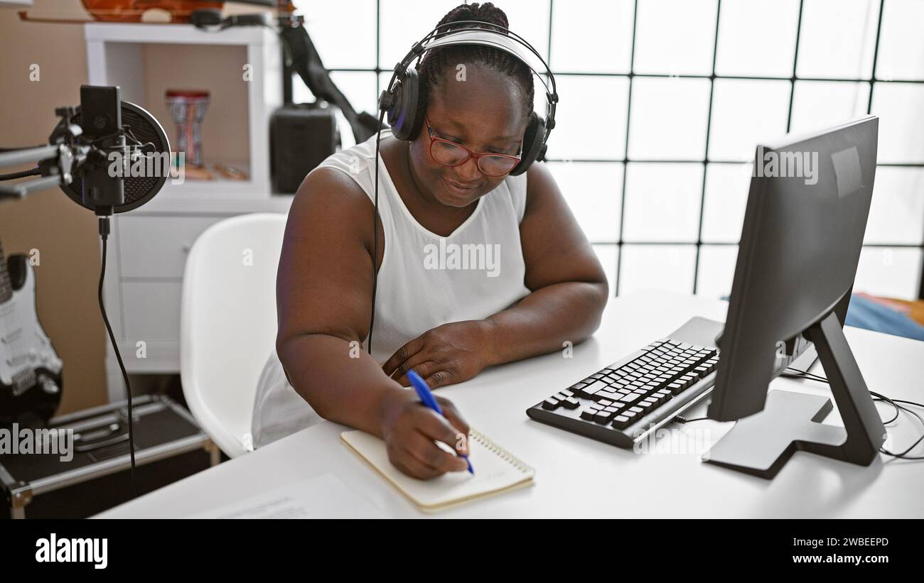 Smiling african american woman, a confident musician, composing a soulful song in a music studio, engrossed in her musical world. Stock Photo