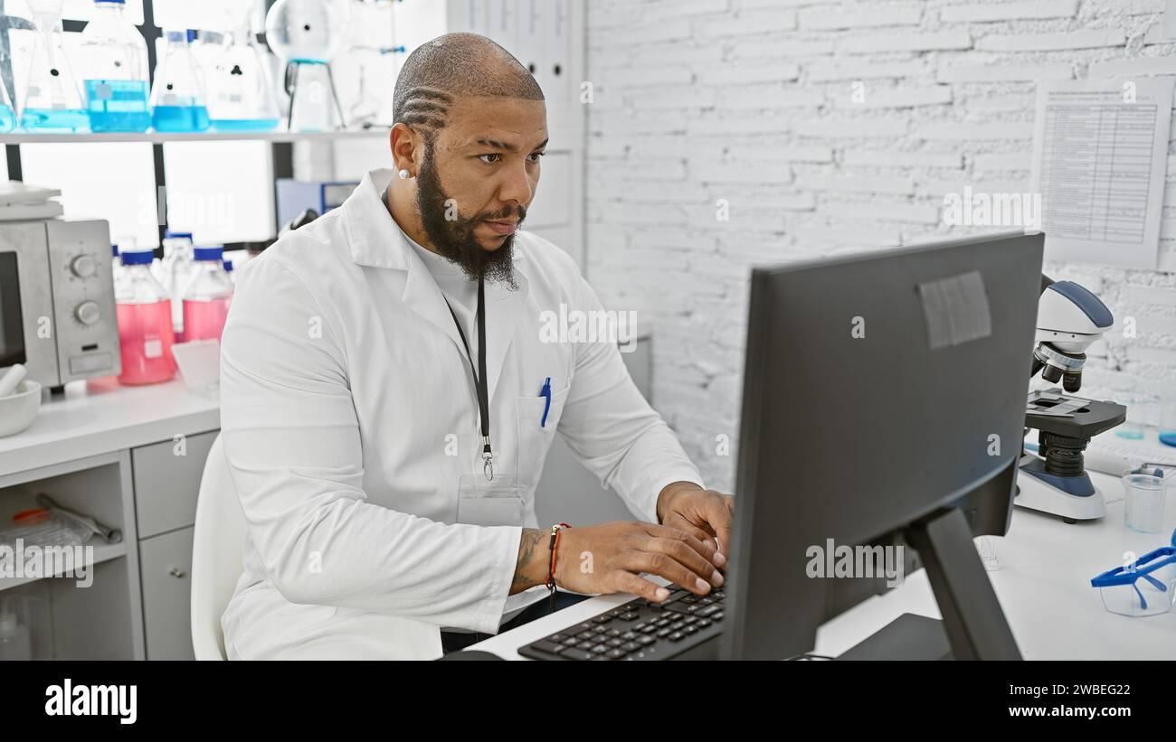 African man in white lab coat working on computer in modern laboratory ...