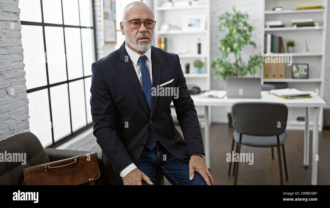 Confident mature businessman with beard in modern office, wearing glasses and blue suit. Stock Photo
