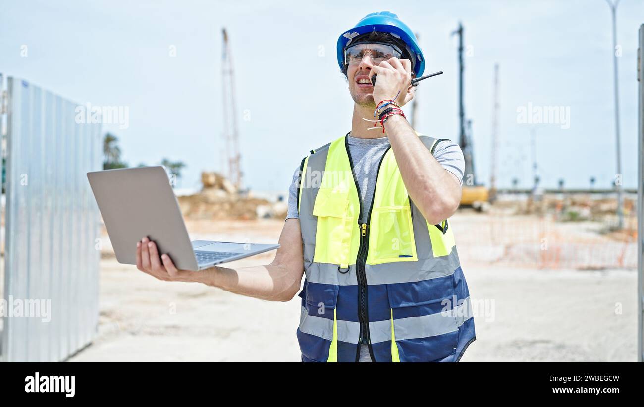 Young hispanic man architect talking on walkie-talkie using laptop at construction place Stock Photo