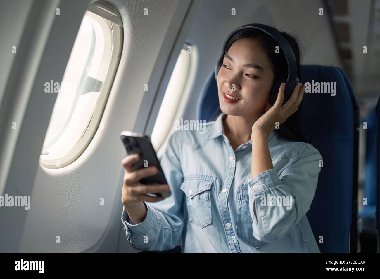 Asian woman traveler in airplane wearing headset listening music from mobile phone going on a trip vacation travel concept Stock Photo