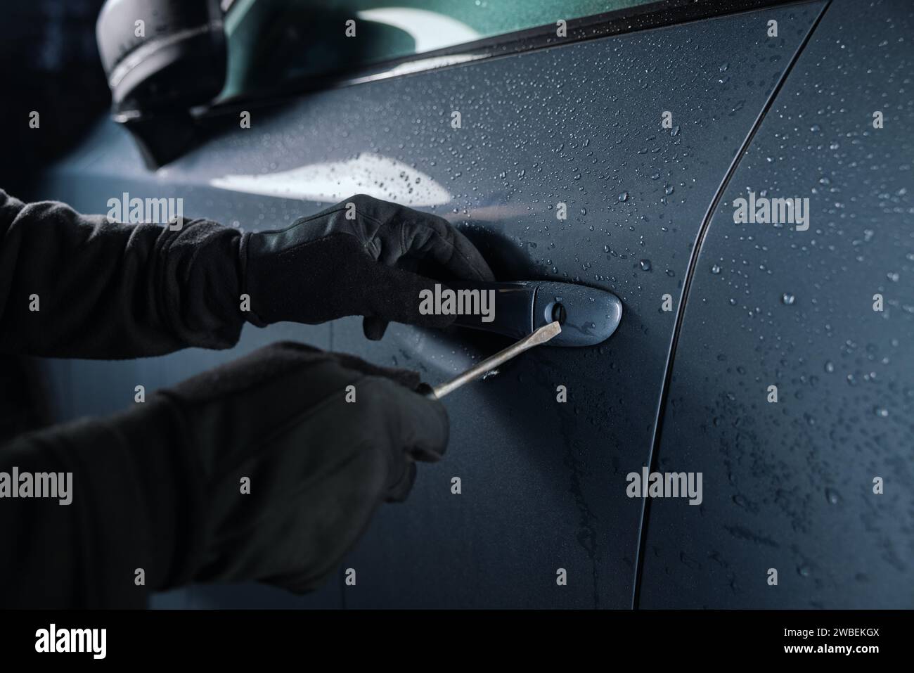 car thief with screwdriver break a door lock and steal a vehicle at night Stock Photo