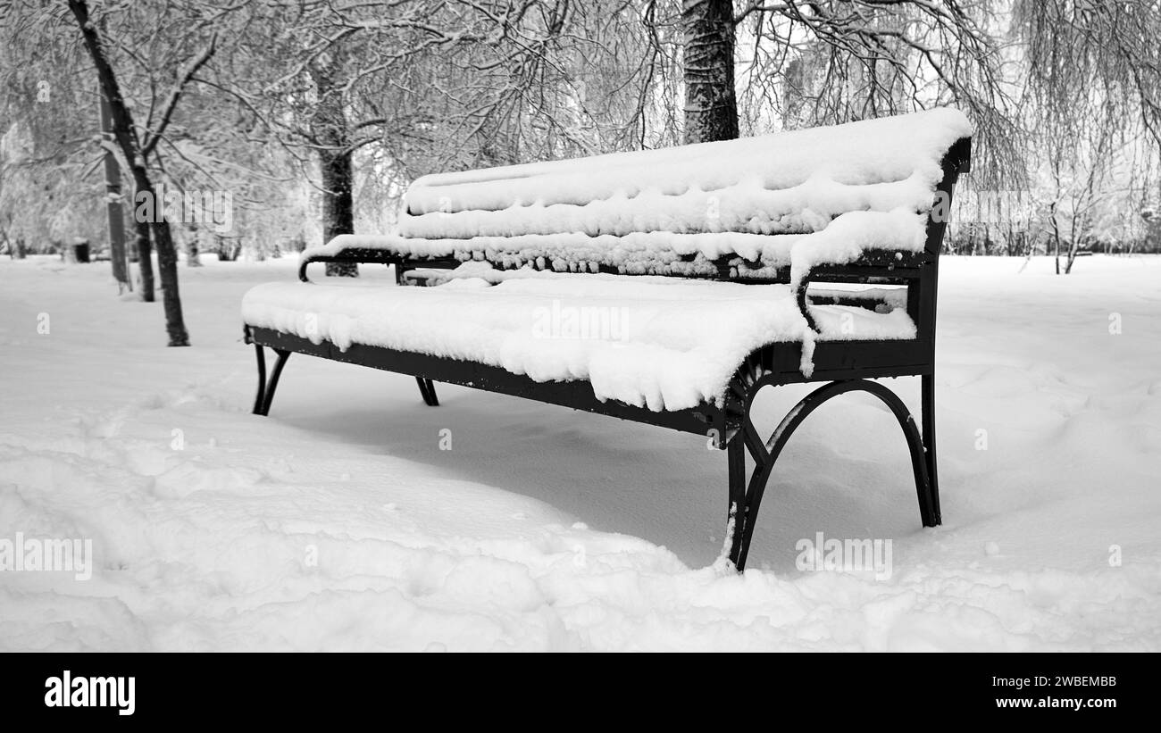 Black and white photo of a park bench covered with snow Stock Photo