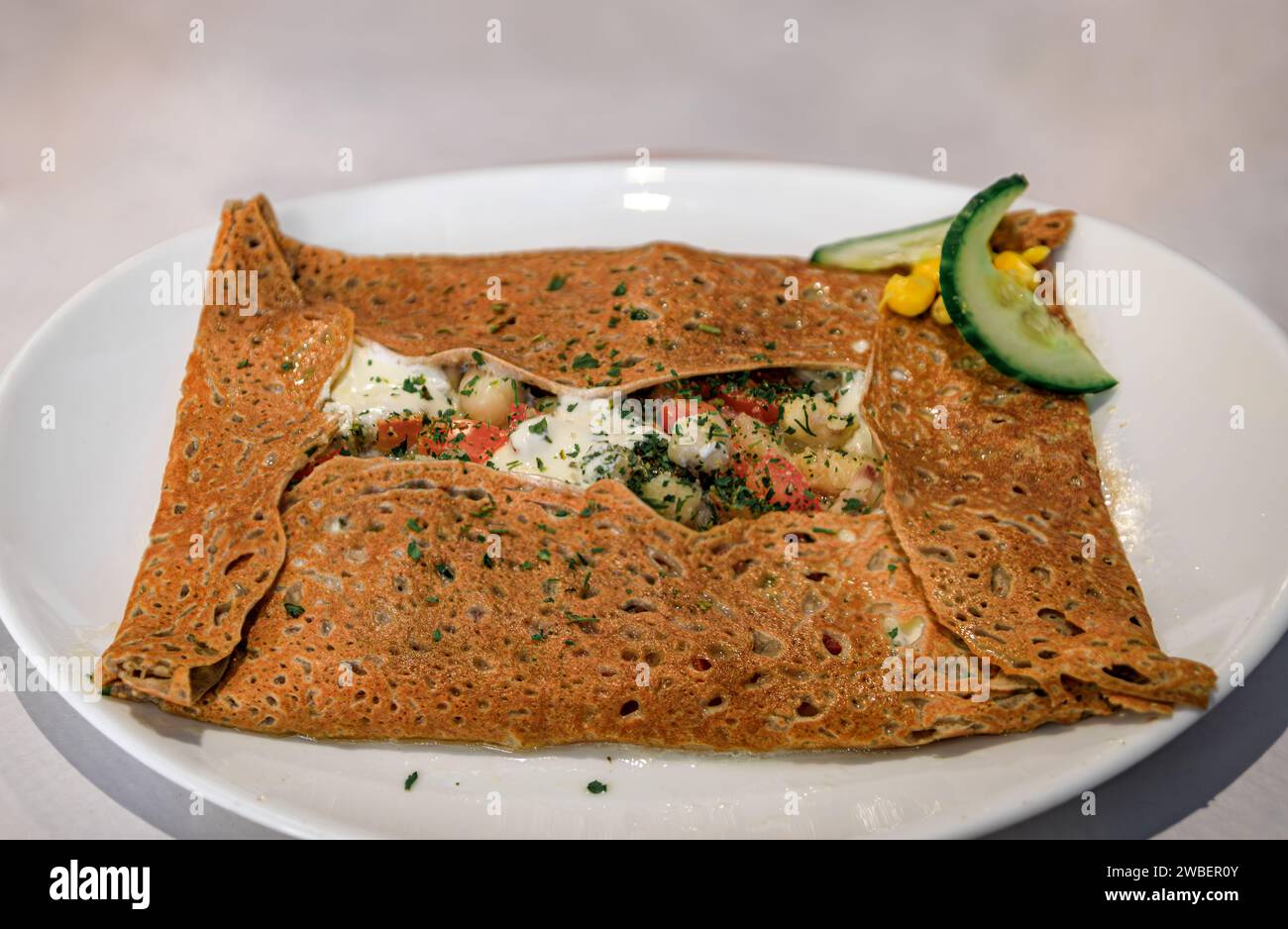 French specialty, buckwheat crepe with frog legs, tomatoes and cheese at a winstub restaurant in Colmar, France, Alsatian Wine Route village Stock Photo