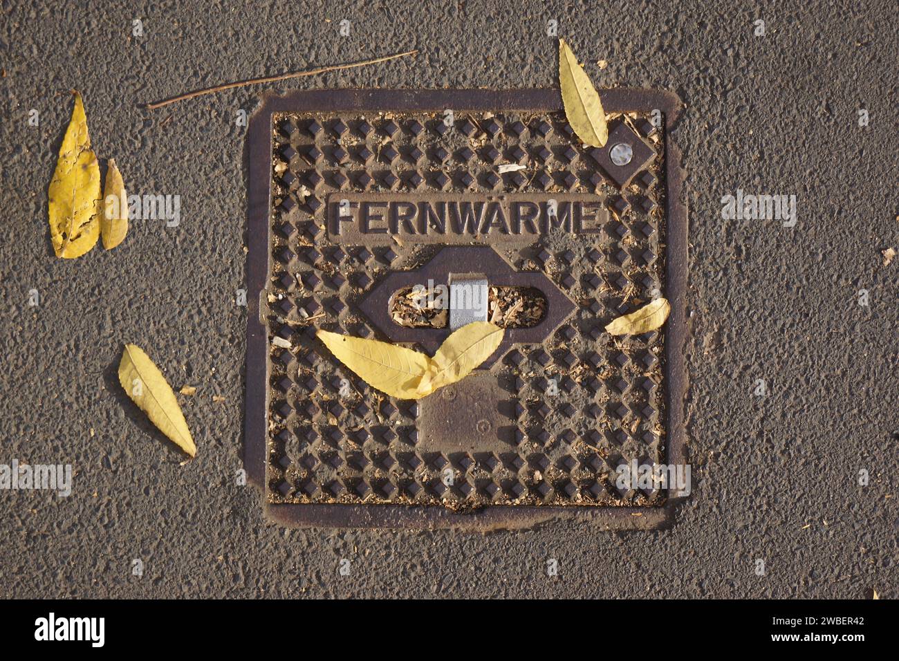 On the sidewalk, you can see the cover of a shut-off valve for district heating, called Fernwaerme in Germany. Stock Photo