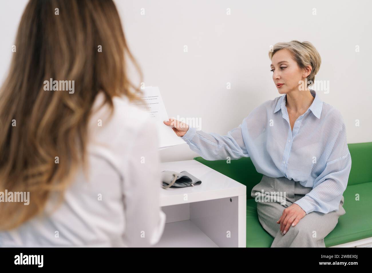 Rear view of unrecognizable woman doctor in white uniform giving paper ...