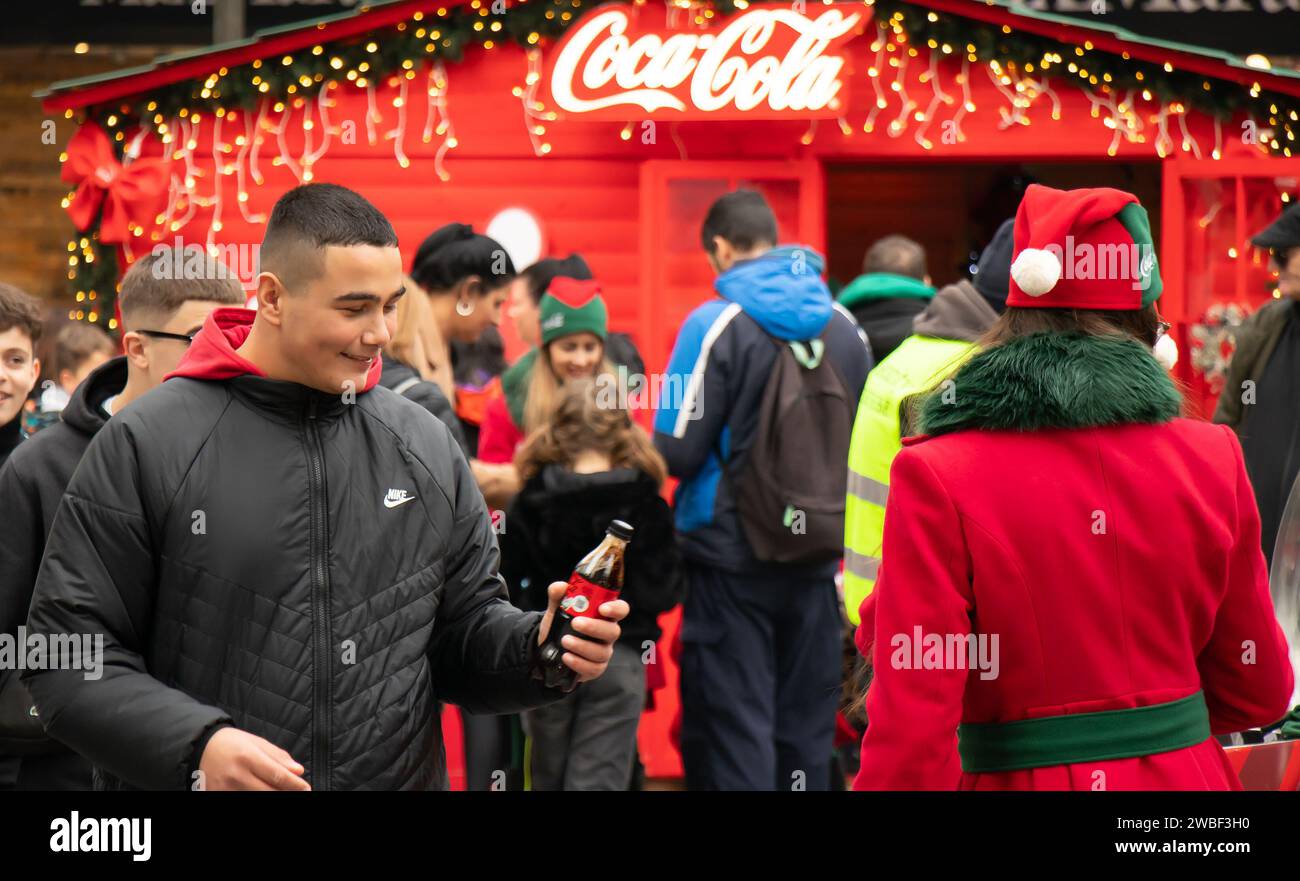 Belgrade, Serbia - January 5, 2024: Teenage boy receiving a bottle of Coke during Coca Cola promotion campaign on city street during Christmas holiday Stock Photo