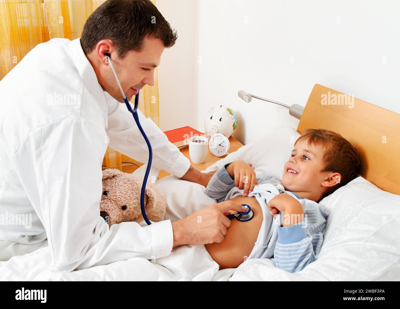 A doctor on a house call examines a sick child. Little boy lying in bed, 4-6 years old, stethoscope, examination, cold, flu Stock Photo