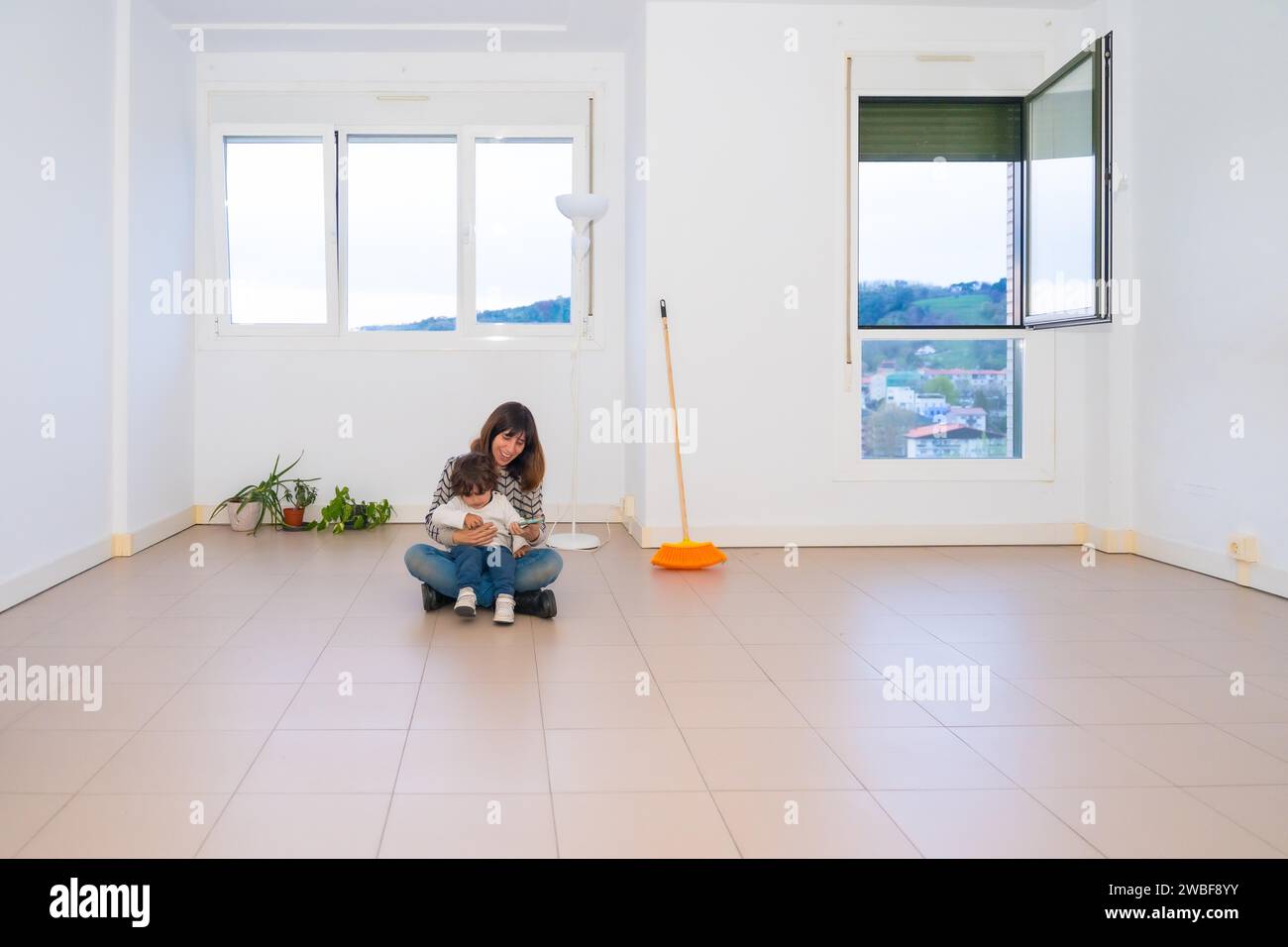 Mother and child sitting in the middle of an empty house after moving Stock Photo