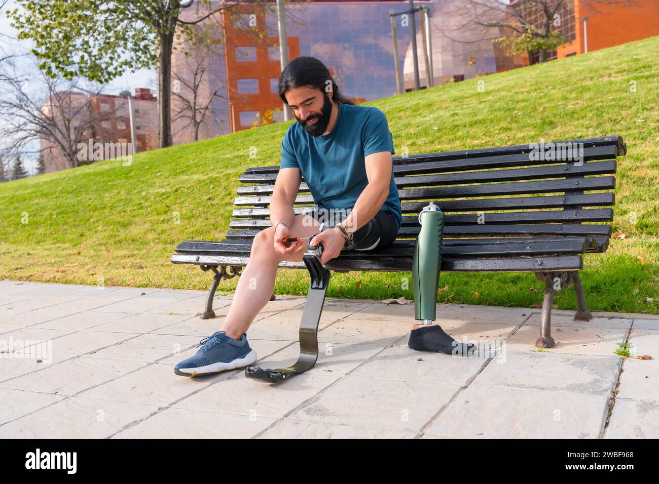 Physically disabled man adjusting prosthetic leg before running sitting on an urban park bench Stock Photo