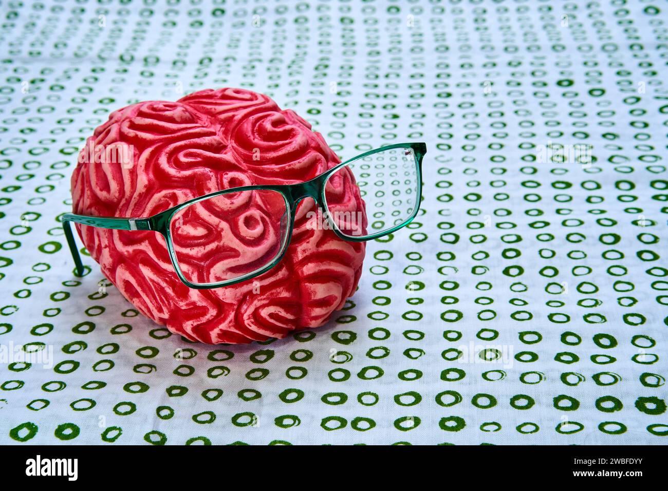 Representation of a red human brain with green glasses on a greenish surface. Stock Photo