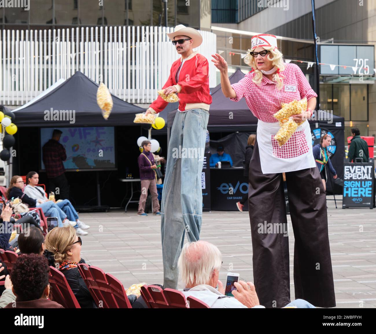 Performers on stilts throwing popcorn at attendance at outdoor film showing Stock Photo