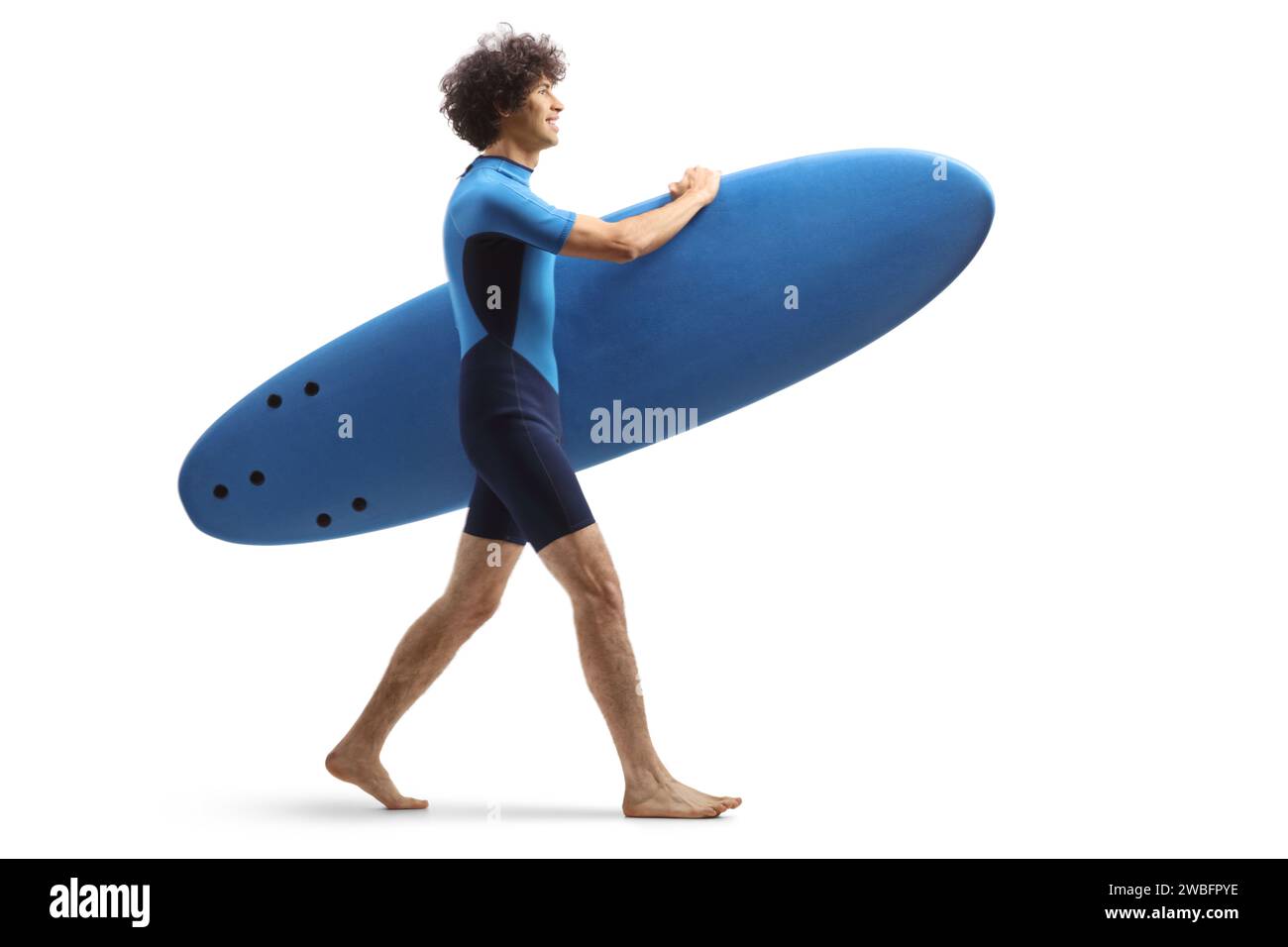 Full length profile shot of a guy in a wetsuit walking and carrying a surfboard isolated on white background Stock Photo