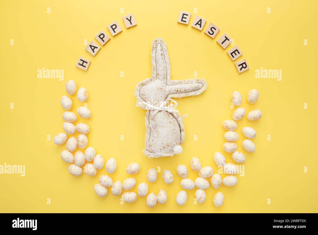 Handmade Easter decor, stylish Easter eggs, textile rabbit on yellow background. Easter wreath shape Stock Photo