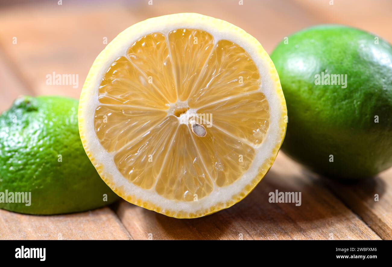 Half Cut Fresh Lemon with green limes on either side, on a wooden cutting board. Stock Photo
