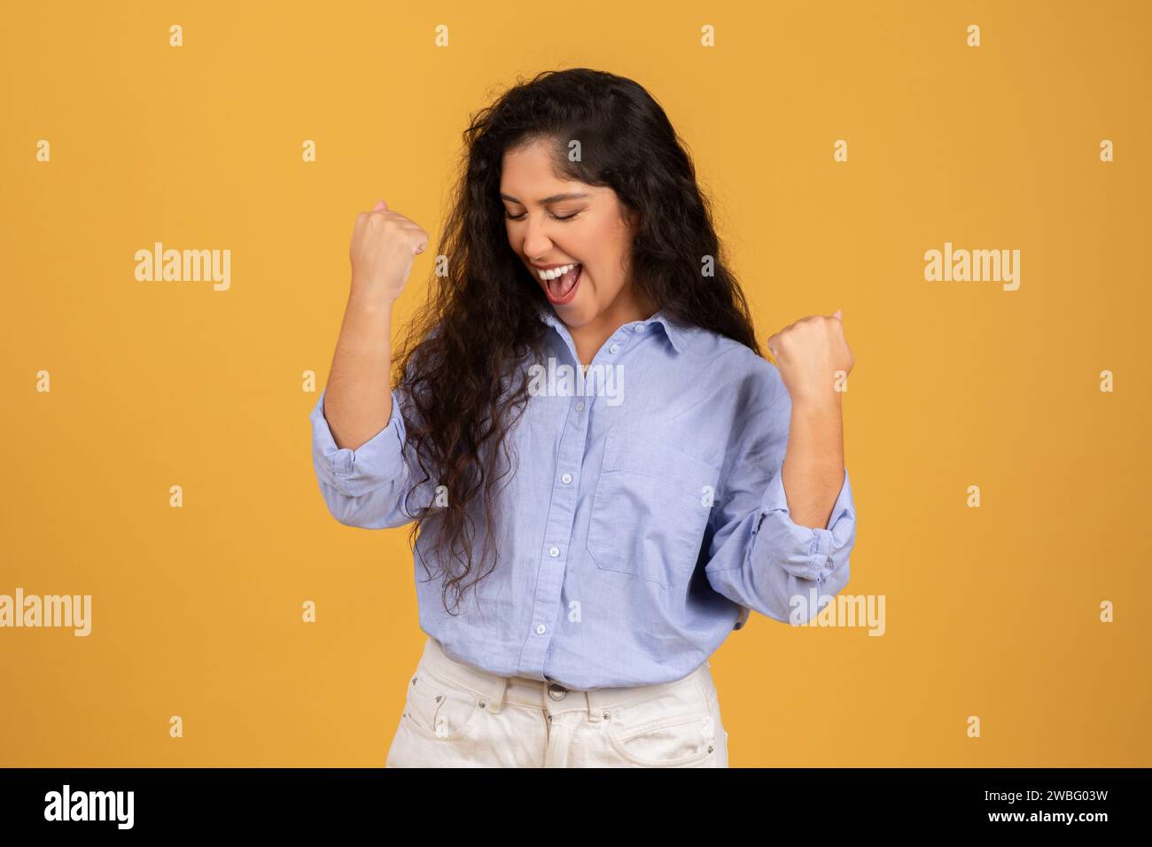 Exuberant young woman with long curly hair, wearing a blue blouse Stock Photo