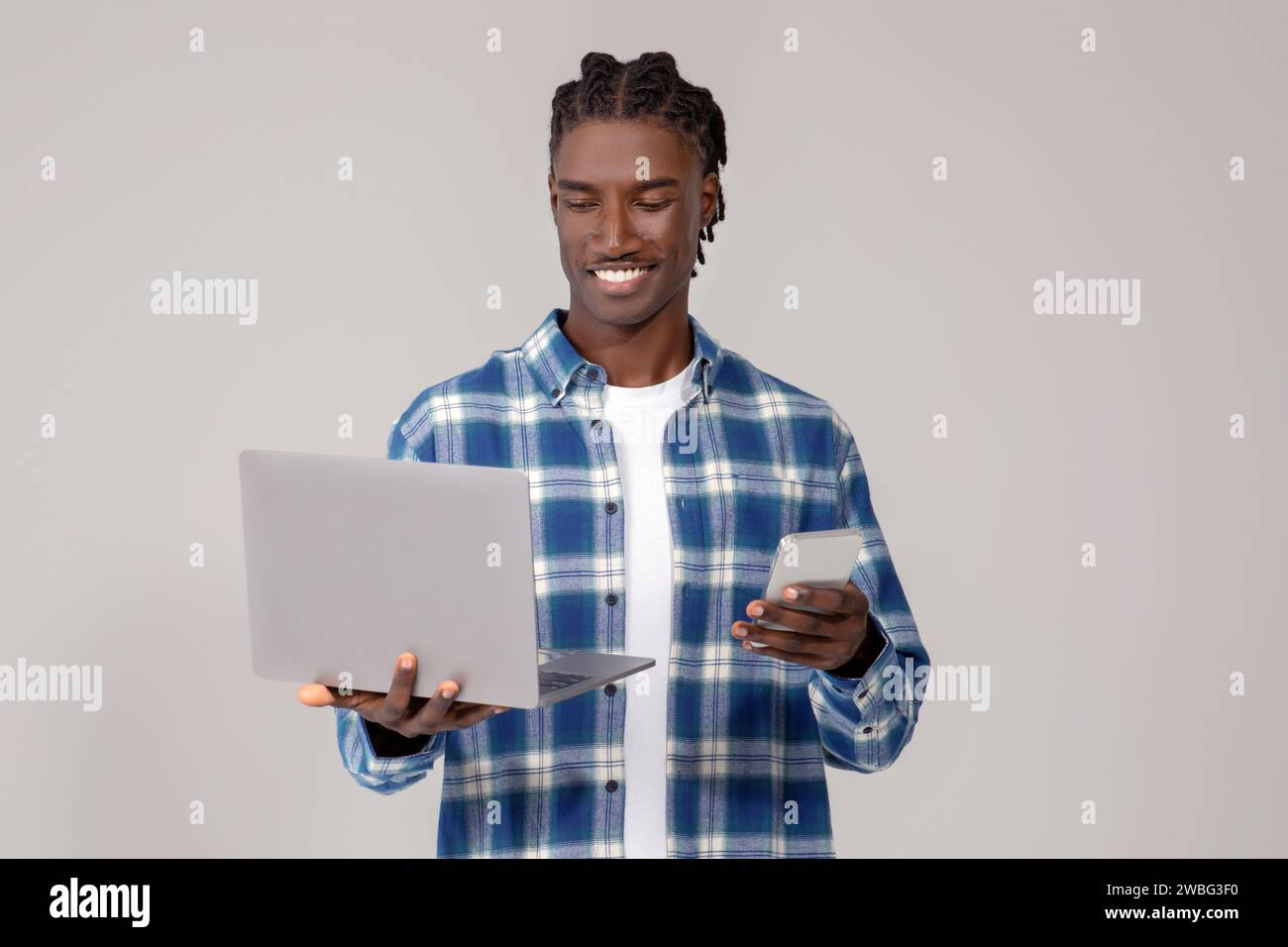 Focused young black man using laptop and holding smartphone Stock Photo