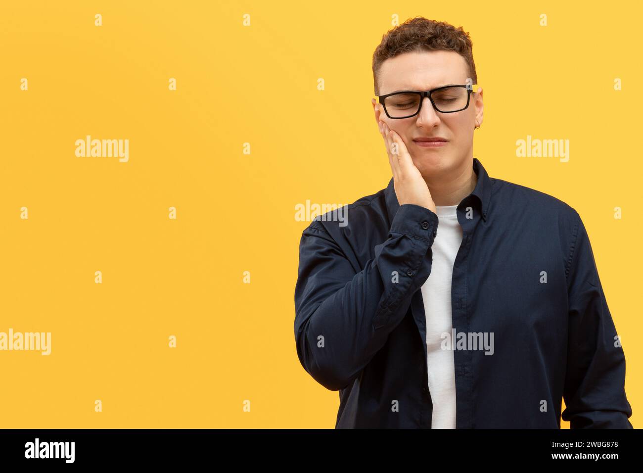 Unhappy young european guy holding hand on cheek Stock Photo