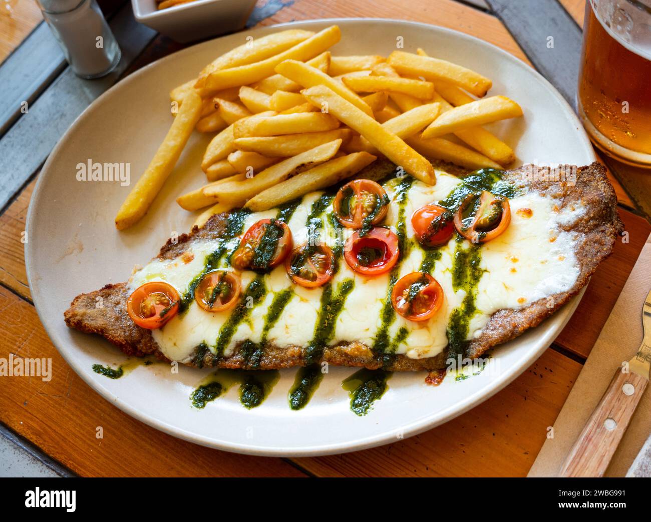 Beef steak with mozzarella, tomatoes and pesto served with fries Stock Photo