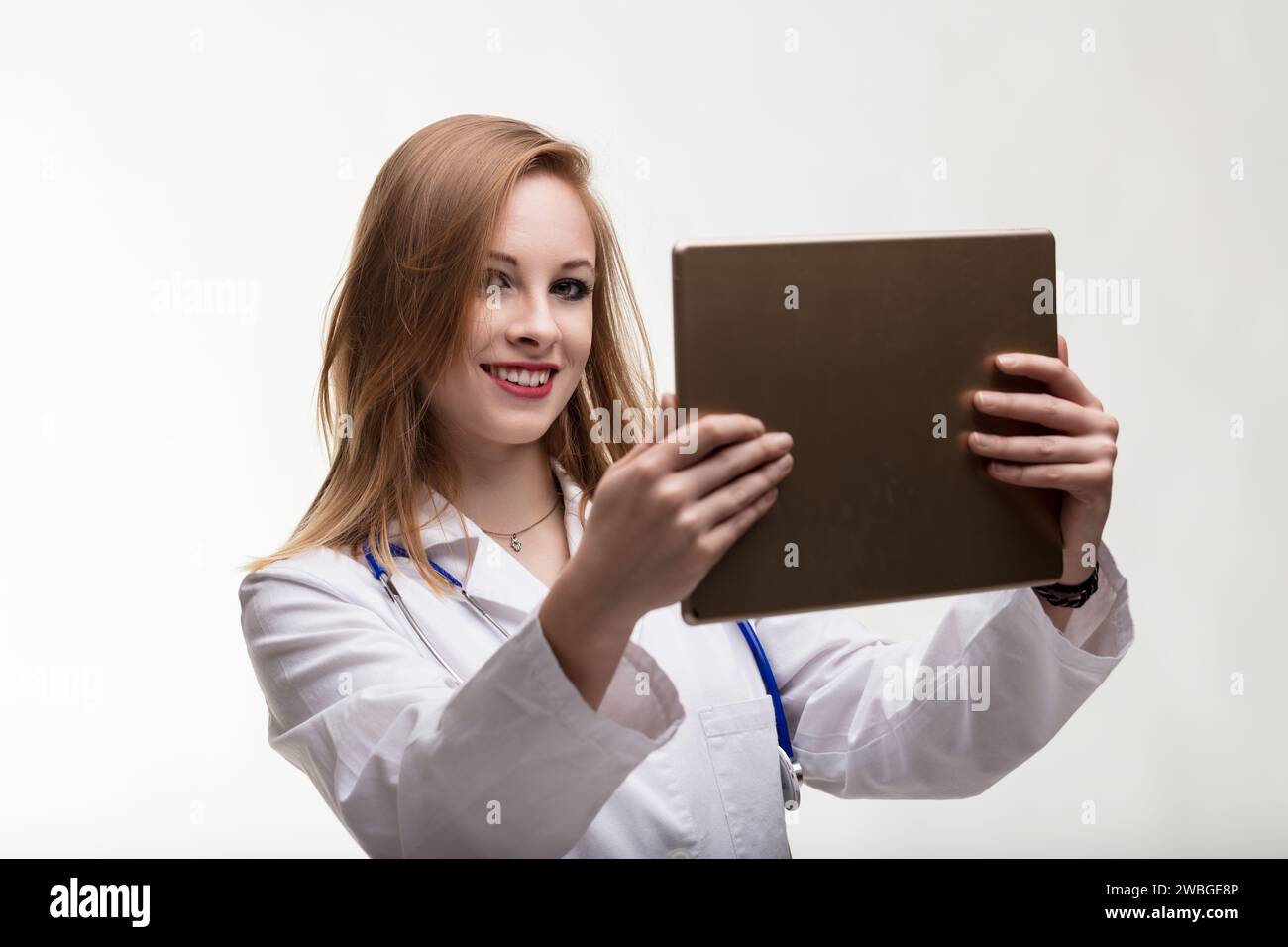 Engaged and tech-savvy doctor reviews patient information on a digital device, smiling Stock Photo