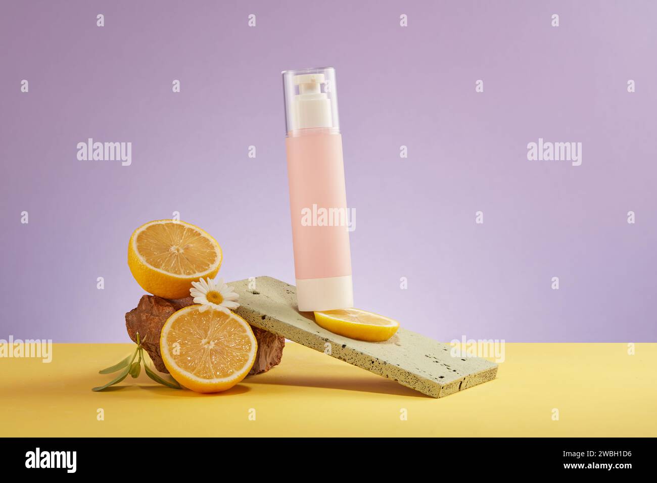 Pink bottle mockup for cosmetic, half of lemon and stone displayed on purple background. Lemon is high in vitamin c which boosts collagen and improves Stock Photo
